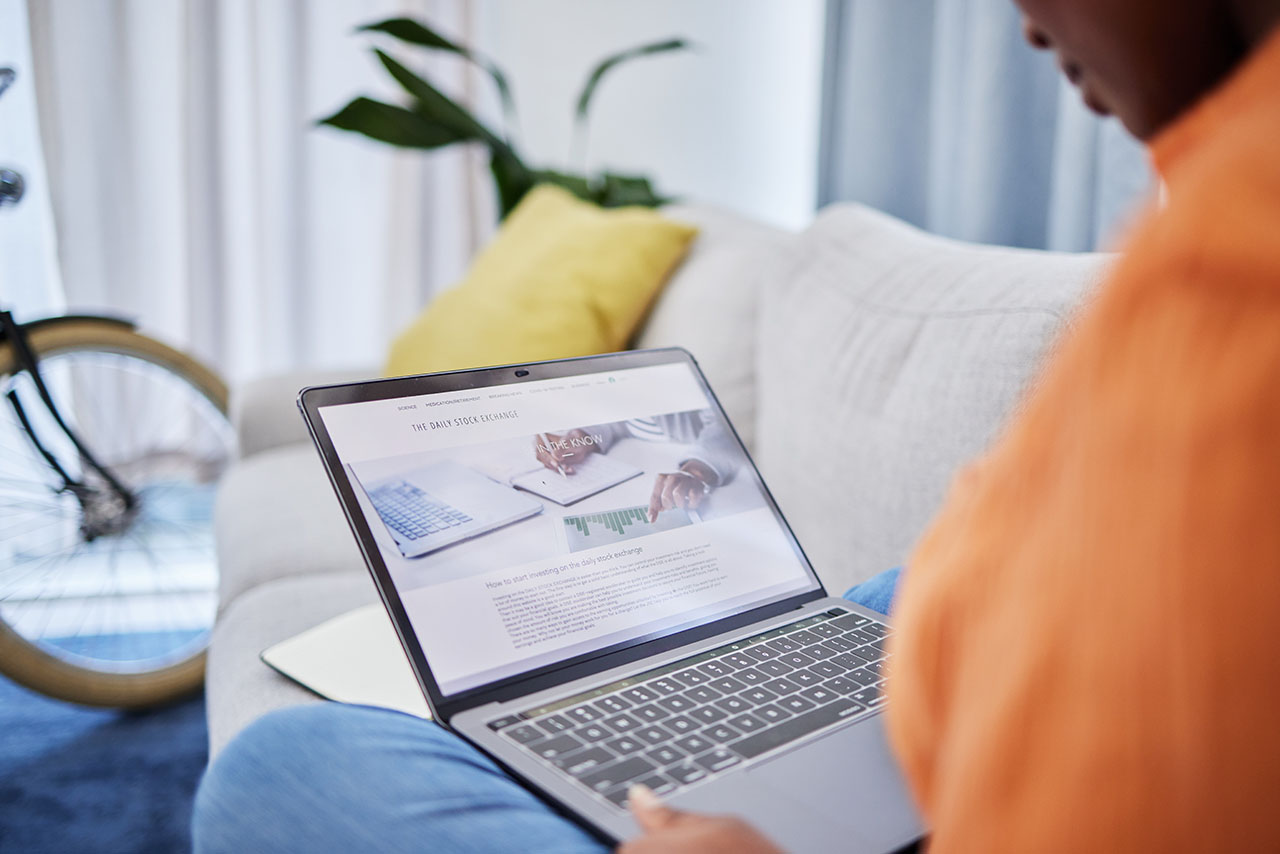 Laptop screen, stock market and person on sofa in work from home